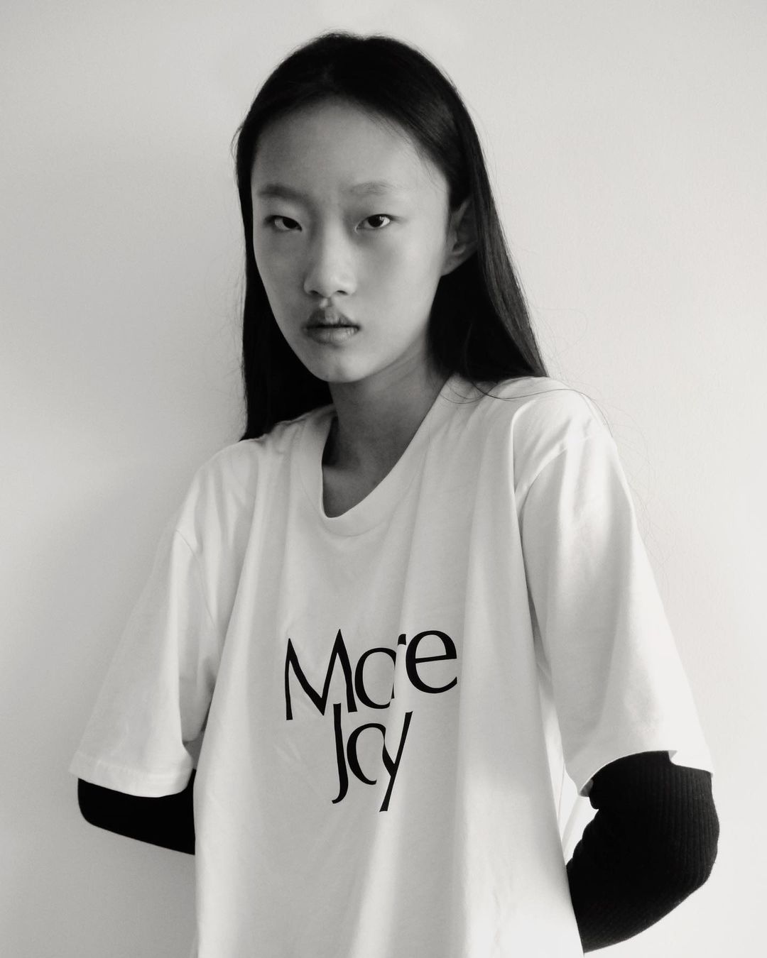 Monochrome portrait of an east asian woman wearing a white t-shirt over black sleeves against a plain white background
