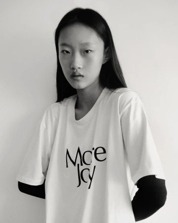Monochrome portrait of an east asian woman wearing a white t-shirt over black sleeves against a plain white background