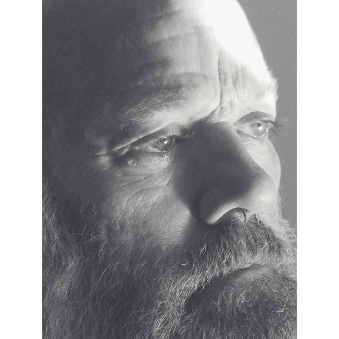 Black and white portrait of a mature man with a beard, focusing on his face and contemplative expression in soft, diffused lighting.
