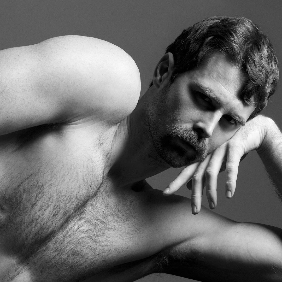 Striking black and white portrait of a muscular adult male with a mustache, resting his head on his arm against a plain background.
