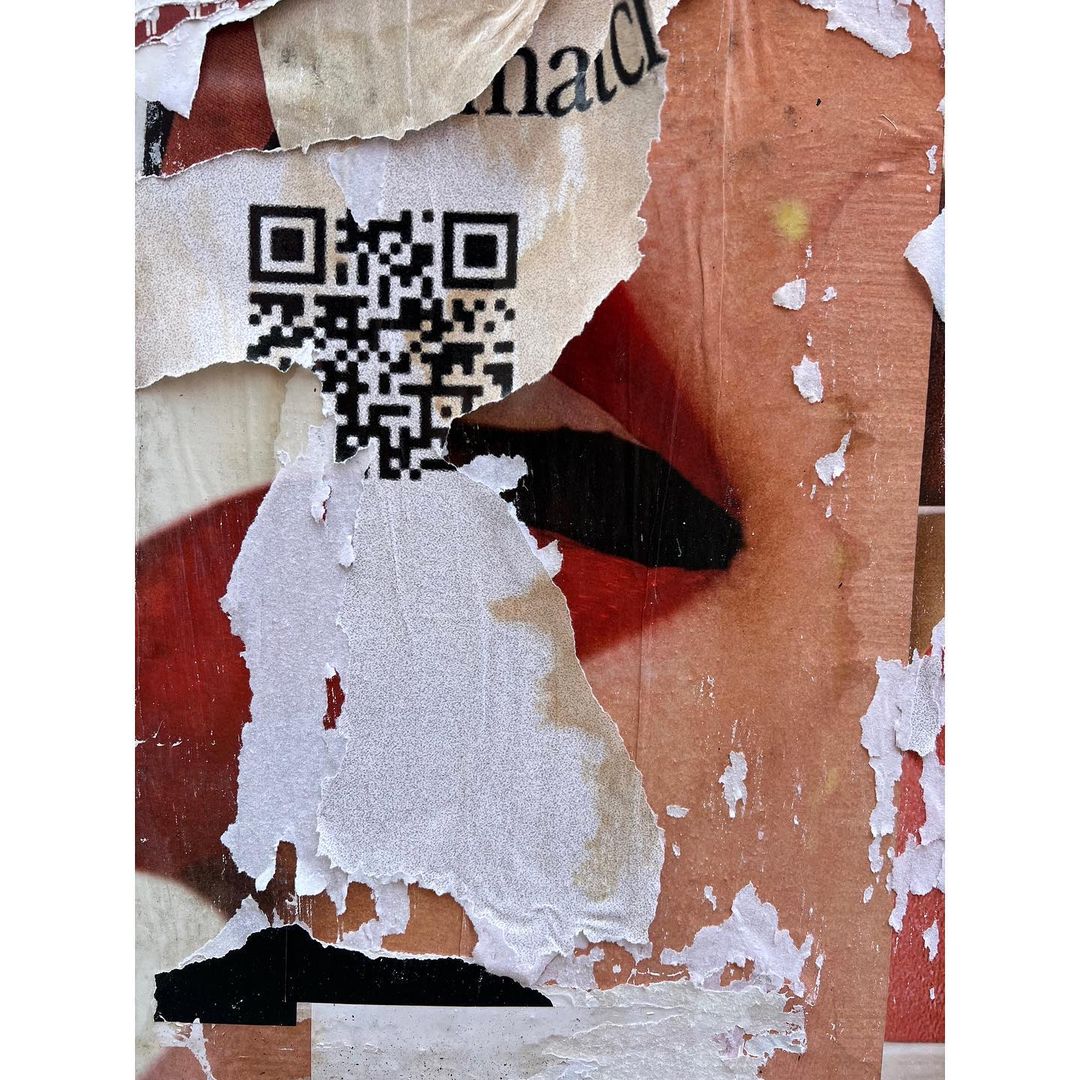 Closeup of a textured wall with torn posters, revealing layered colors, a QR code, and abstract patterns, creating an urban aesthetic.