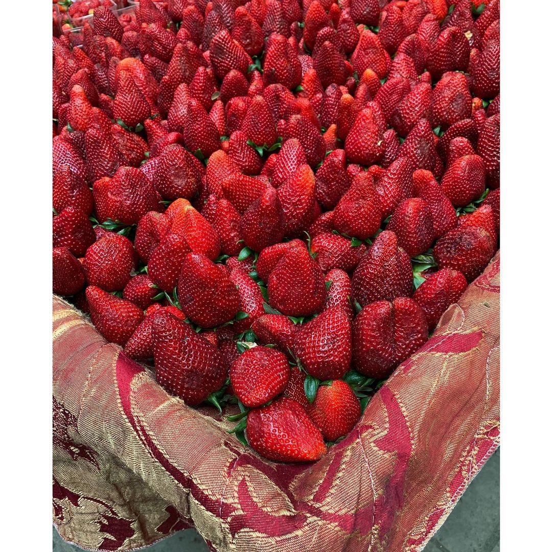 Close-up of fresh ripe red strawberries arranged on a red and gold patterned cloth. The strawberries are piled high, filling the frame.