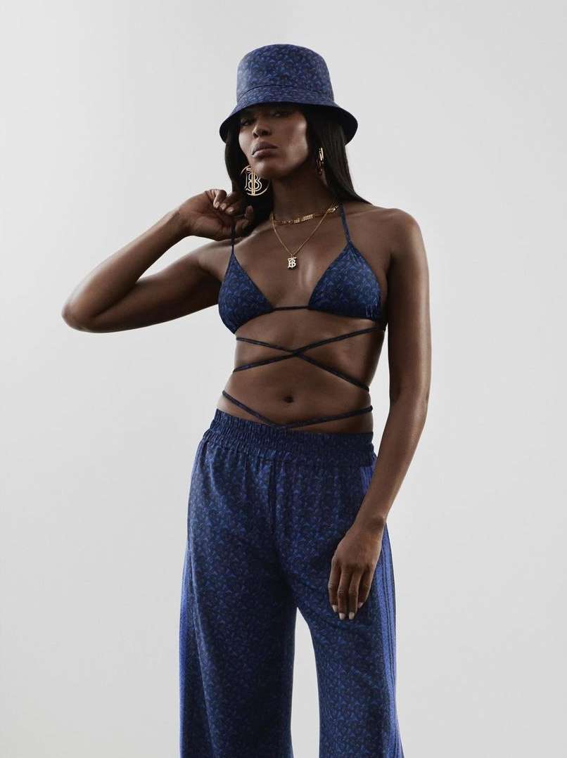 An adult female fashion model posing in a shiny, blue, glittery bikini top, bucket hat, and matching pants on a white studio backdrop.