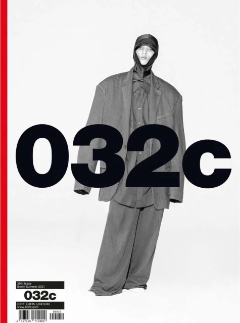 Magazine cover featuring a person in an oversized suit and head covering in front of a bold black and white title, with a red stripe.