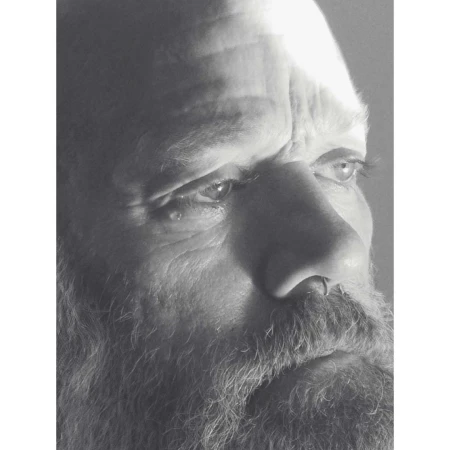 Close-up monochrome portrait of a bearded older man with a nose ring looking pensively