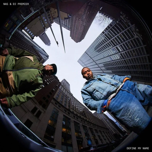 Two men pose in an urban setting with tall buildings and sky visible in the background with a fisheye lens creating a circular perspective.