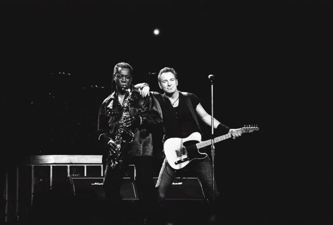 Black and white photo of Bruce Springsteen with a guitarist alongside Clarence Clemons playing a saxophone during live music performance.