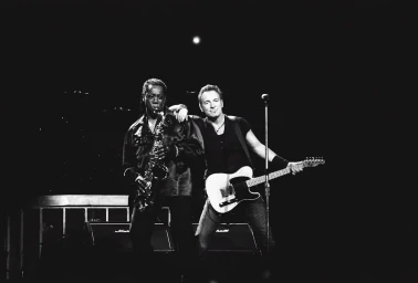Black and white concert photograph of Clarence Clemons playing saxophone and Bruce Springsteen holding an electric guitar.