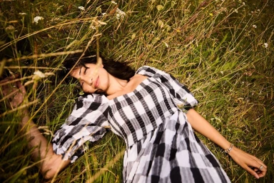 Woman lying in tall grass wearing a black and white gingham dress photographed by Danny Craven