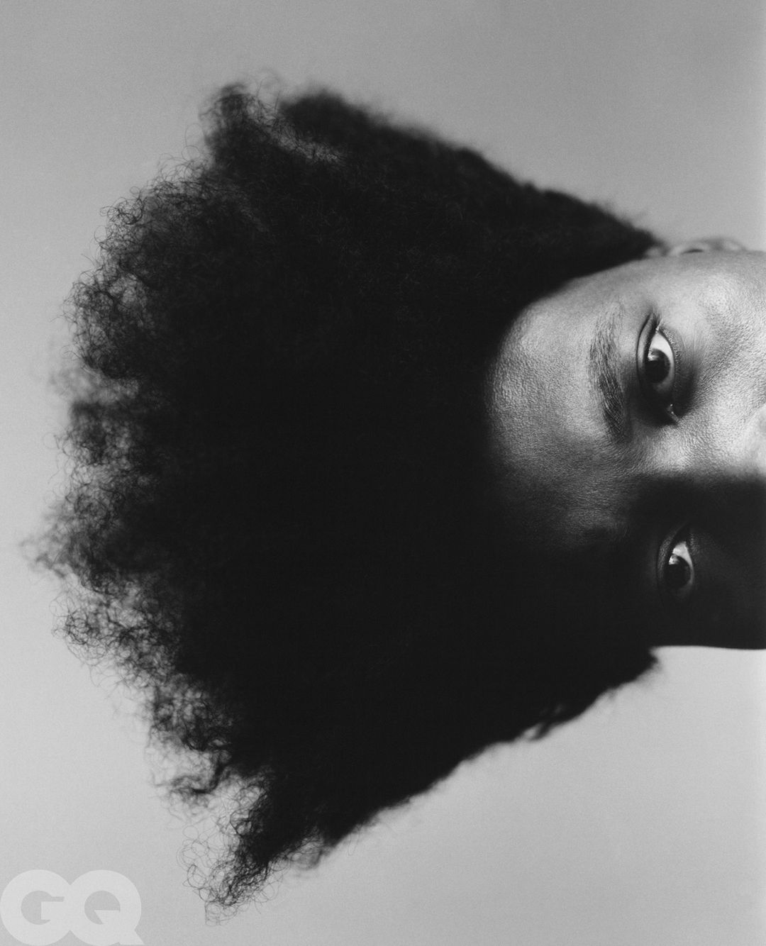 Portrait of an adult with dark skin and afro hairstyle, gazing directly at the camera in a black and white studio shot.