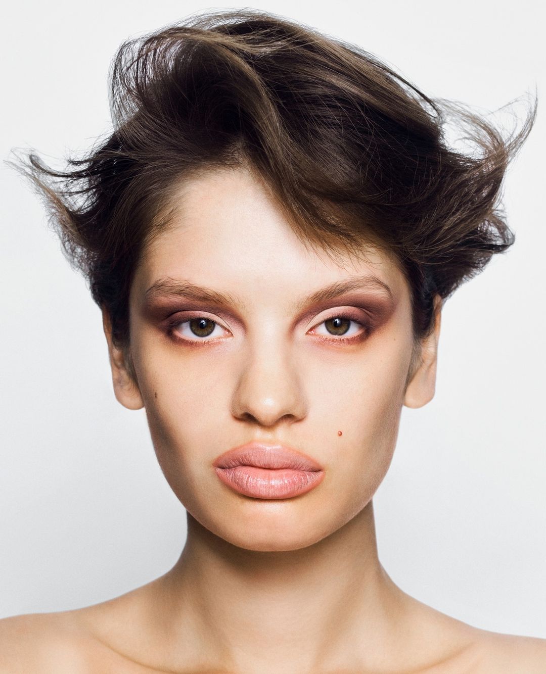 Close-up portrait of a brunette woman with light skin and brown eyes wearing brown eyeshadow against a white background in a photo studio.