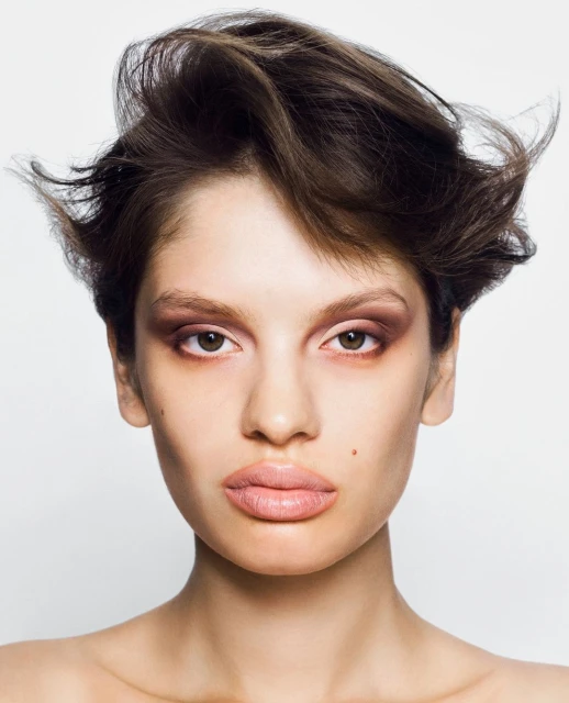 Close-up portrait of a brunette woman with light skin and brown eyes wearing brown eyeshadow against a white background in a photo studio.