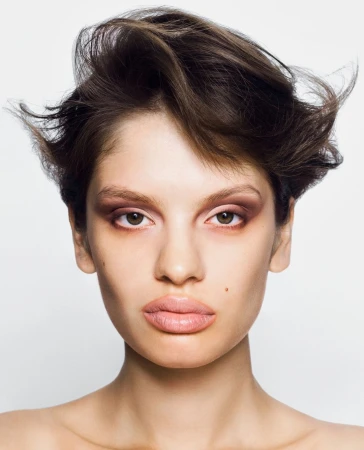 Close-up portrait of a brunette woman with light skin and brown eyes wearing brown eyeshadow against a white background in a photo studio.