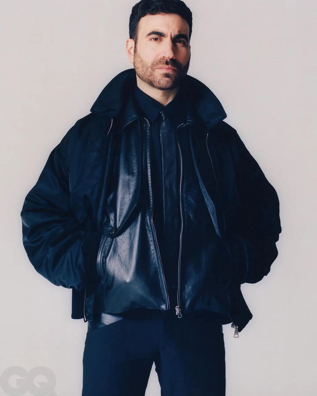 Portrait of a man wearing a black button-down shirt and a black bomber jacket in front of a plain white backdrop.