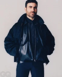 Brett Goldstein portrait by Danny Lowe in dark jacket and shirt against a plain background