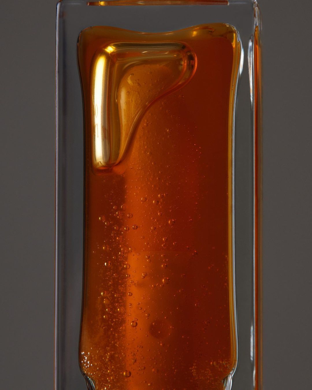 Close-up shot of a clear rectangular bottle filled with viscous amber liquid, possibly honey or oil, showcasing its texture and color.