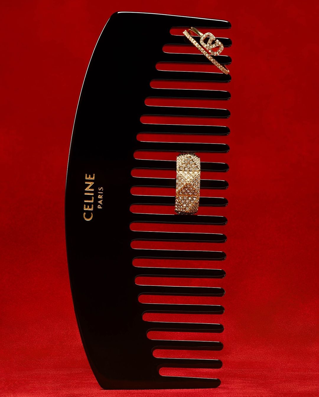 A black comb is displayed on a red background with golden accessories. The comb has the brand name CELINE PARIS printed on the side.
