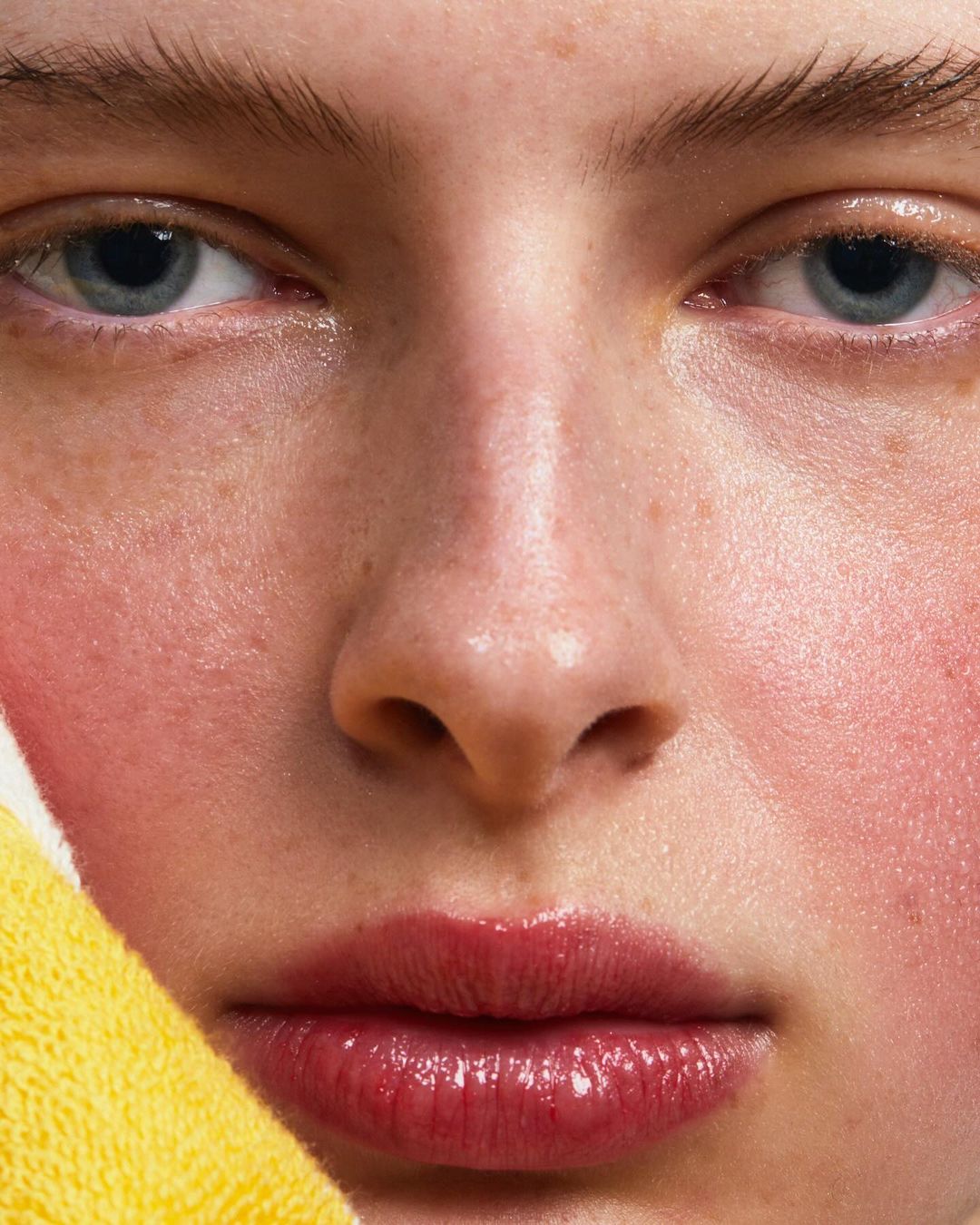 Close-up portrait of a young fair-skinned woman with blue eyes and red lips, featuring a yellow towel in the foreground, and soft lighting.