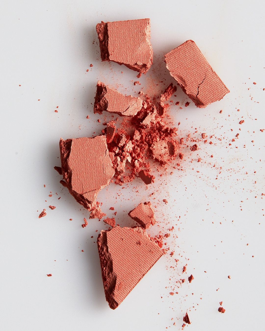 Broken blush powder on white background. Cosmetic product shards and dust create abstract pattern. Makeup photography.