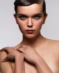 Portrait of a woman with dark wet-look sculpted hair and winged eyeliner posing with hands crossed near shoulders