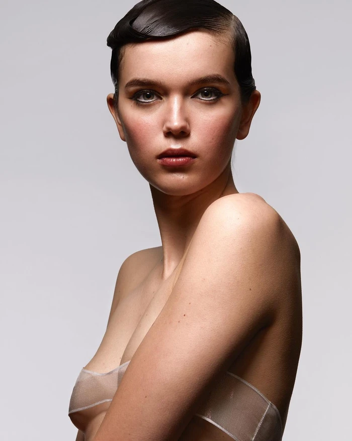 Portrait of a woman with sculpted dark hair and sheer strapless garment against a light grey background