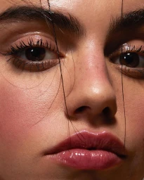 Extreme close-up portrait of a woman face with glossy pink lips, dark eyelashes, and stray strands of hair falling across her nose.