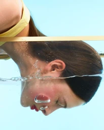 Close-up profile of a woman underwater with air bubbles rising past her face against a light blue background.