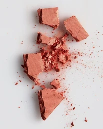 Crushed peach-colored powder cosmetic pieces scattered across a clean white seamless surface viewed directly from above.