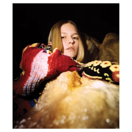Portrait of a young blonde woman wearing a patterned knit sweater leaning over a light textured surface