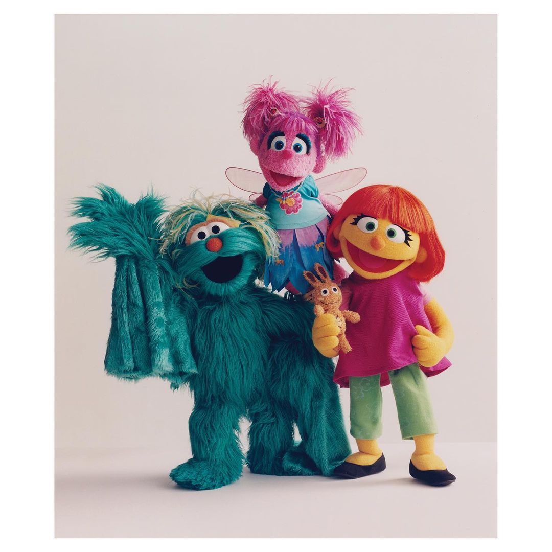 Three Sesame Street puppets, including Abby Cadabby, stand together in a studio setting against a neutral background with bright, soft lighting.