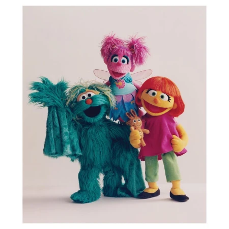 Three Sesame Street puppets, including Abby Cadabby, stand together in a studio setting against a neutral background with bright, soft lighting.