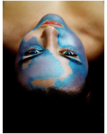 Close-up portrait of a person with artistic blue face paint and red lips, photographed upside down by Dario Catellani.