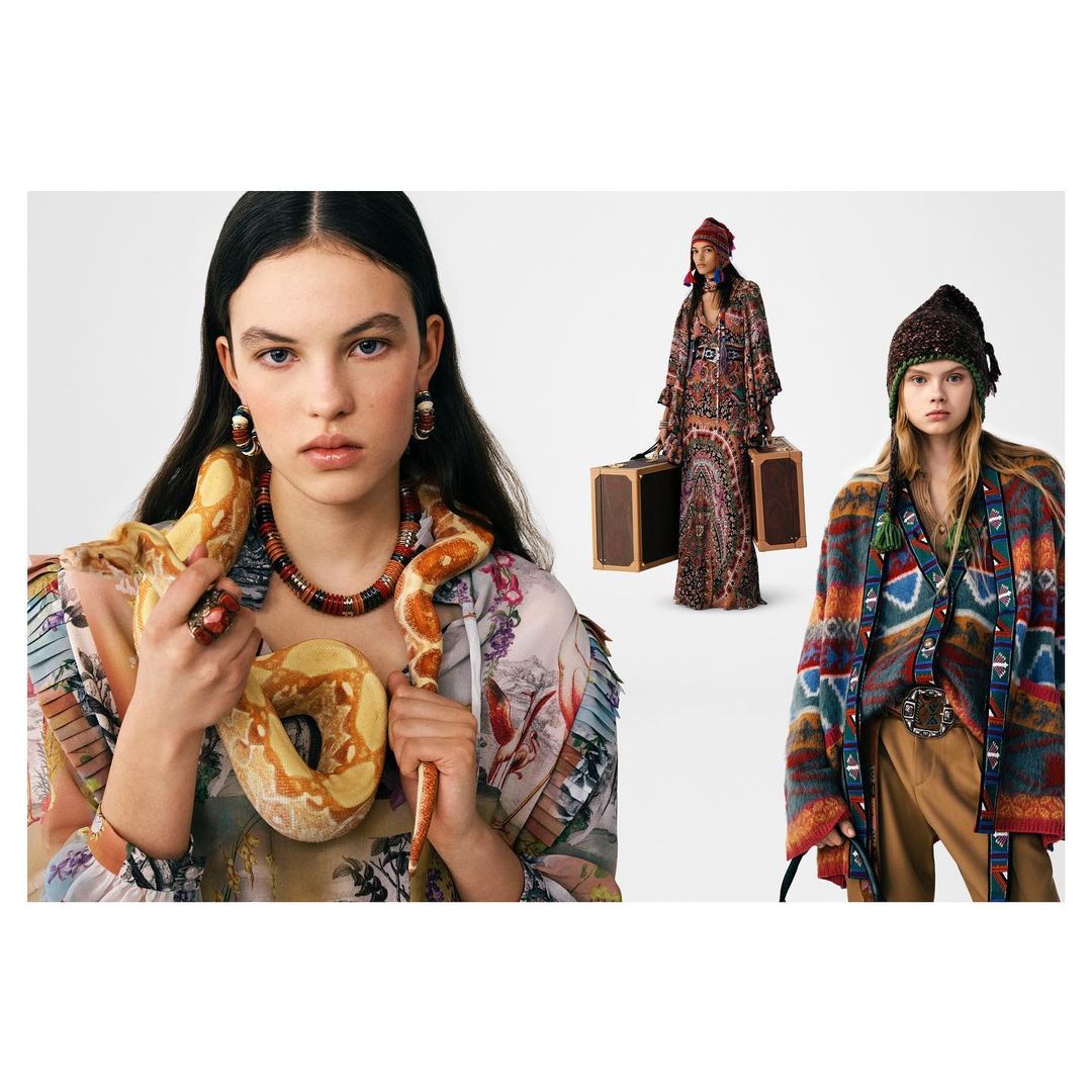 Fashion editorial shot of three women wearing patterned dresses and ornate jewelry, one holding a snake in a studio setting.