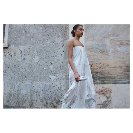 Model in a strapless white draped dress standing outdoors against a textured stone wall
