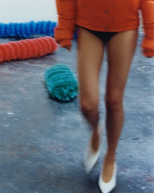 Blurred shot of a human in black bottoms and white shoes walking over a grey floor with colorful textured rollers in the background.