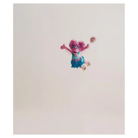 Abby Cadabby, the pink Muppet fairy from Sesame Street, is seen in a full shot against a pale background holding a magic wand.