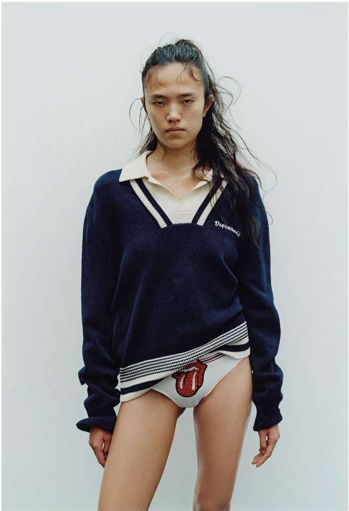 Fashion shot of an Asian woman wearing a navy sweater and underwear with a Rolling Stones logo, standing against a plain background.