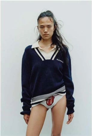 Fashion shot of an Asian woman wearing a navy sweater and underwear with a Rolling Stones logo, standing against a plain background.