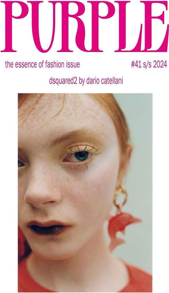 Close-up of a fair-skinned woman with freckles and red hair, wearing dolphin earrings, soft golden eye makeup, and dark lipstick.