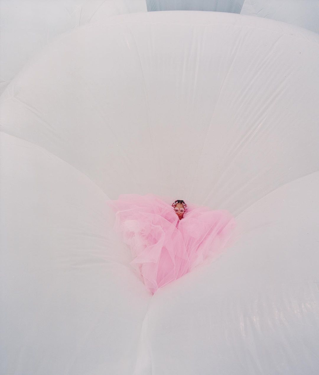 Woman in a pink dress surrounded by large, white inflatable shapes, creating a dreamy, ethereal aesthetic with a unique perspective.