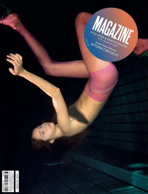 Magazine cover featuring a woman in hosiery and a black top, posing against a dark backdrop with geometric tile patterns.