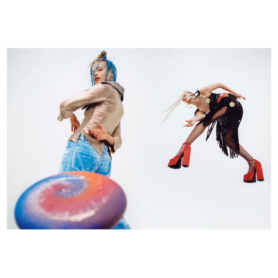 Two women strike dynamic poses in a bright studio, one throwing a colourful disc. The scene is captured with a low-angle perspective.