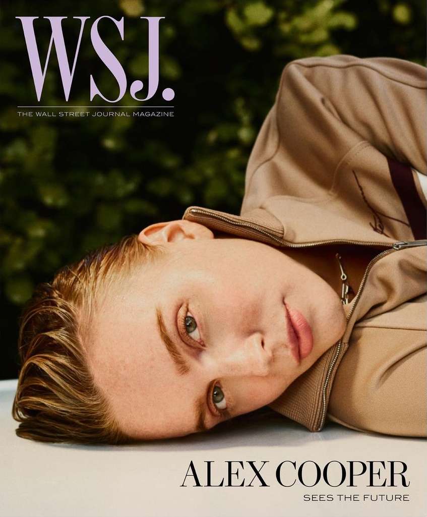 Close-up magazine cover shot of a woman wearing a beige jacket, lying down on a white surface, with a blurred green background.
