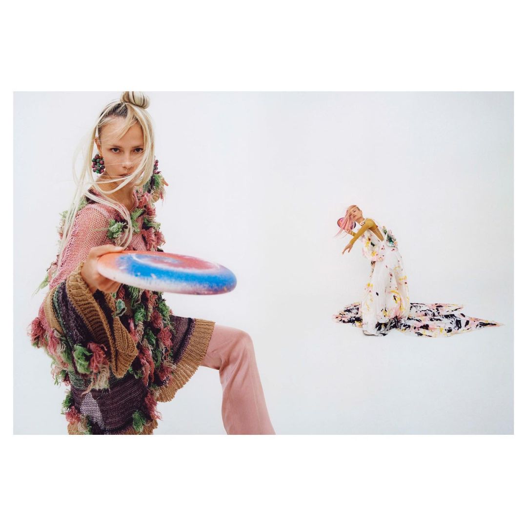 Two women in fashionable outfits are captured in a photo studio setting. One throws a Frisbee, creating a dynamic and engaging visual.