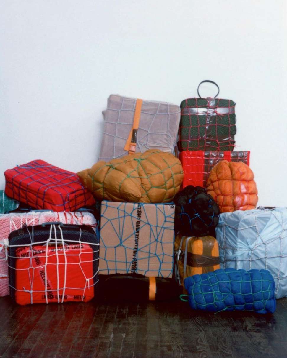Stack of wrapped and bound packages of various sizes and colors tied with string, straps, and netting against a white background.