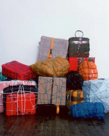 Stack of wrapped and bound packages of various sizes and colors tied with string, straps, and netting against a white background.