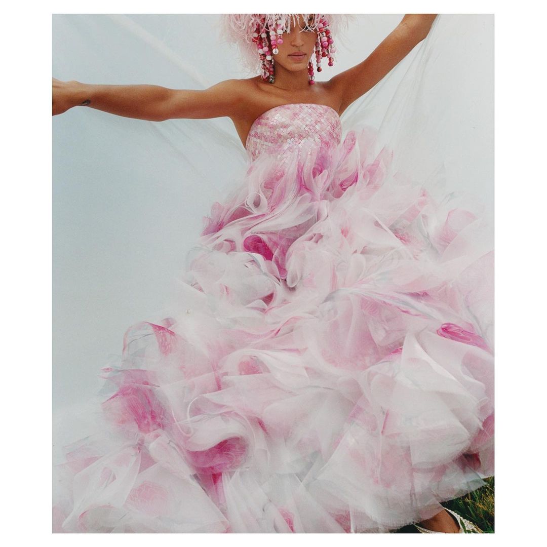 Adult female in a pink and white strapless formal dress and matching headpiece, standing in front of a neutral-toned background.
