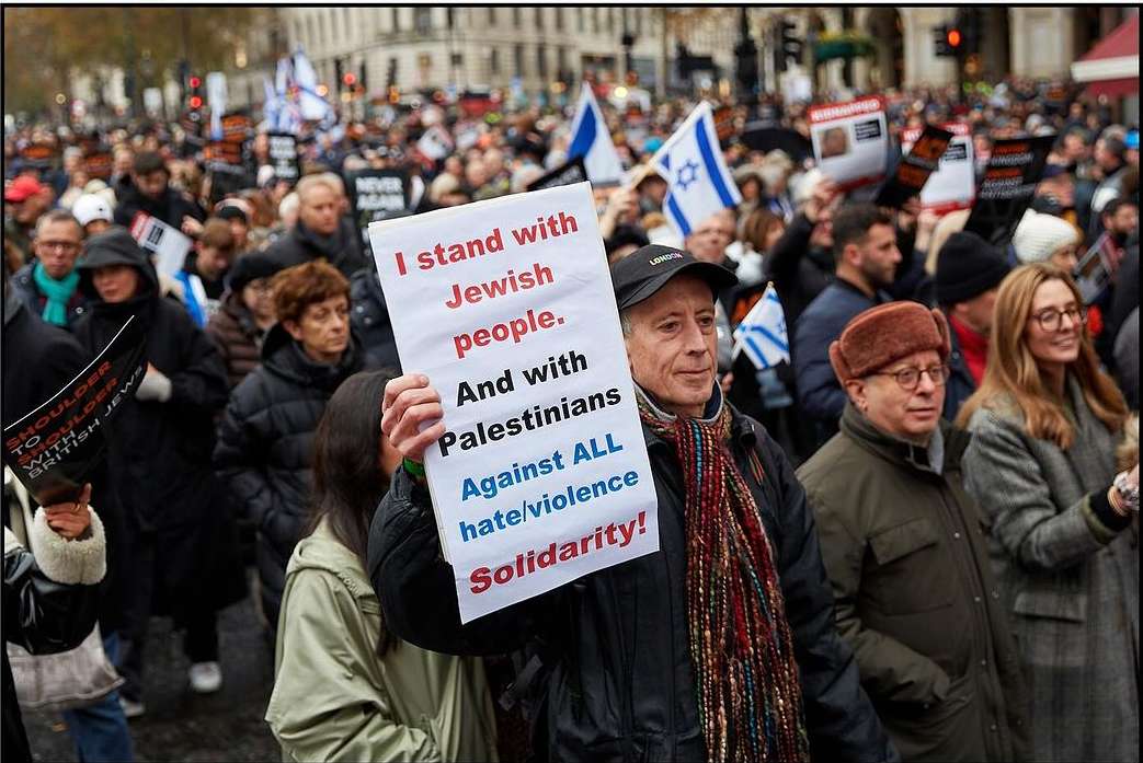 Crowd of people marching in a demonstration, holding signs with political messages, including support for both Jewish and Palestinian people.