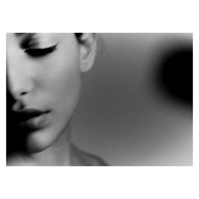 Monochrome close-up portrait of an adult woman with winged eyeliner, soft studio lighting, and blurred background, beauty shot.