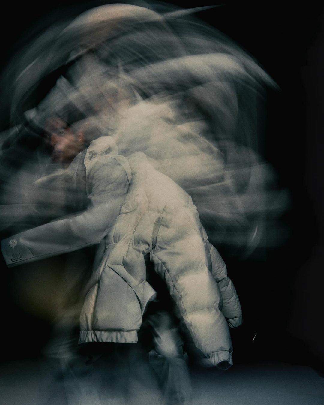 Abstract motion blur of a person wearing a puffer jacket against a dark background, creating an ethereal and dynamic visual effect.